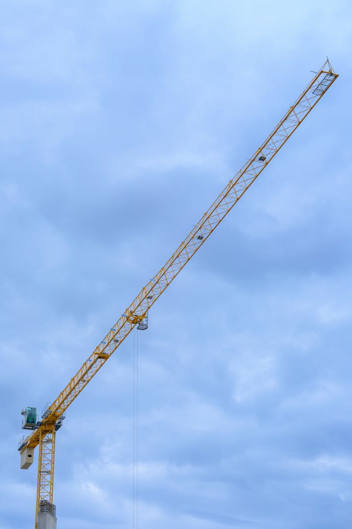 A tower crane extends high against a clear blue sky, symbolizing construction industry power.